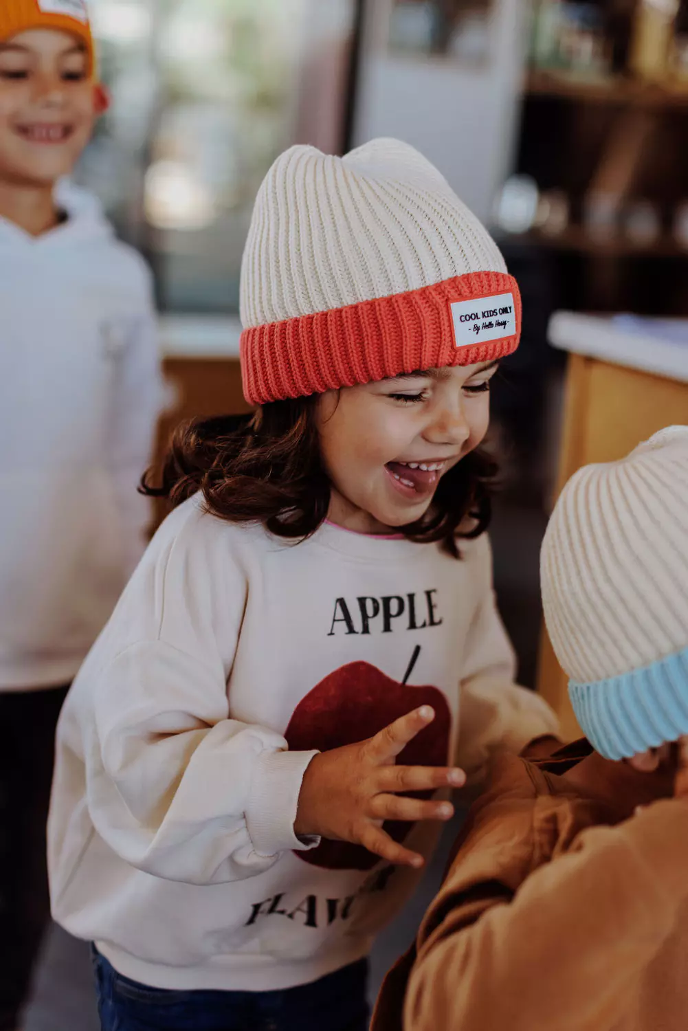 Crianças com gorros de malha branca com barra colorida e camisa com estampa de maçã