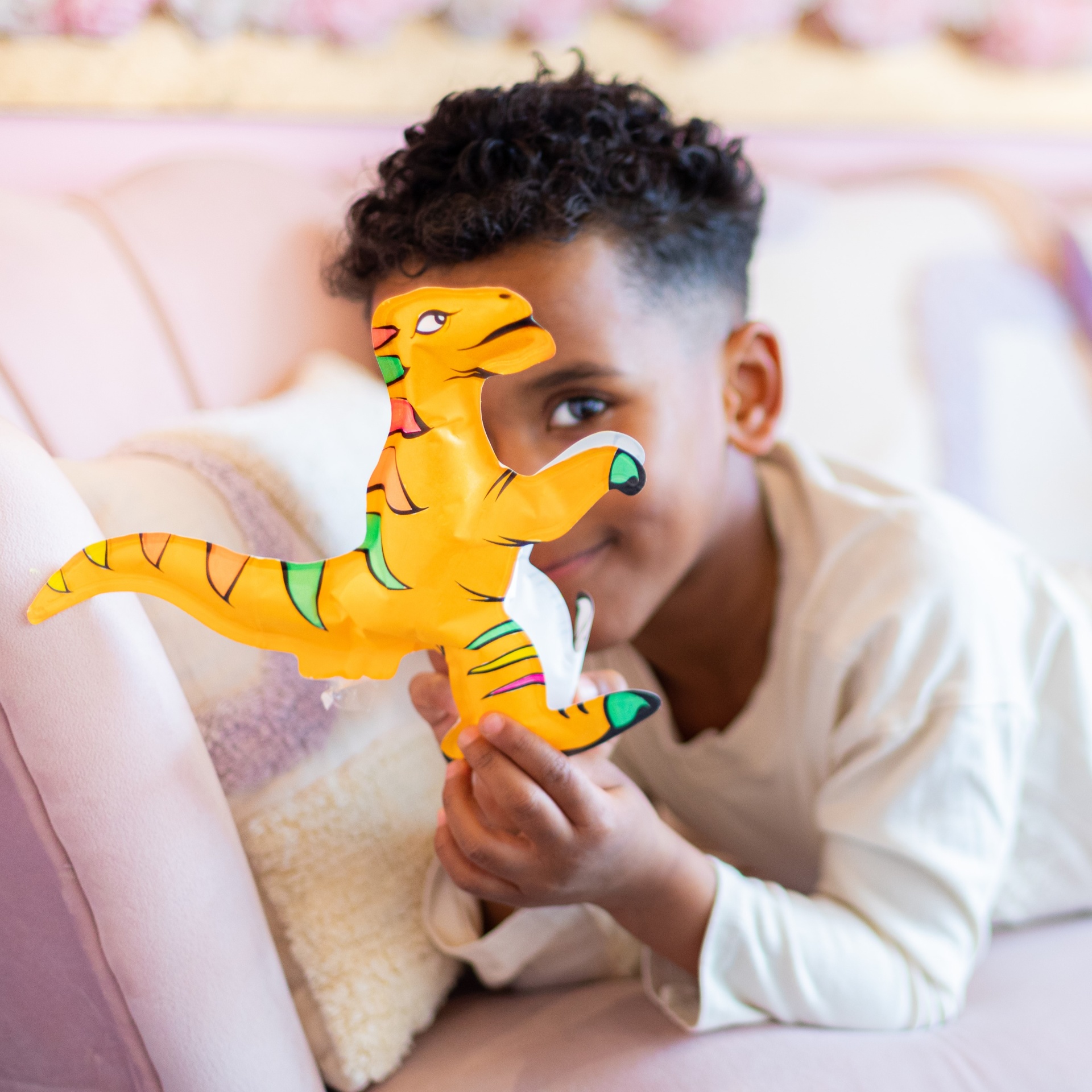 Menino a brincar com brinquedo insuflável dinossauro amarelo no sofá rosa