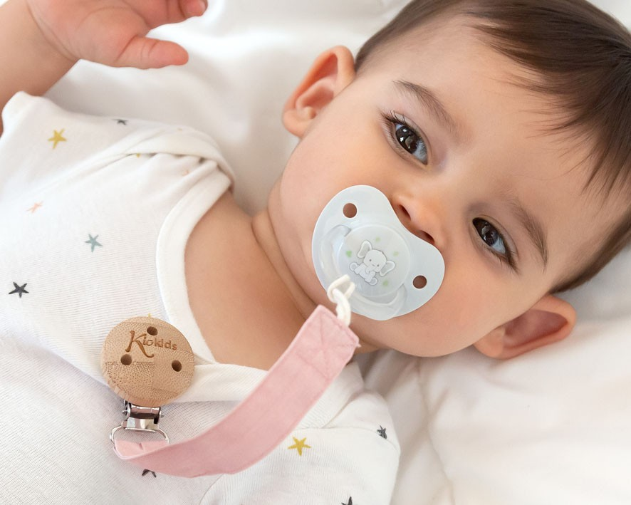 Bebé com chupeta transparente e clip de madeira em body branco com estrelas coloridas