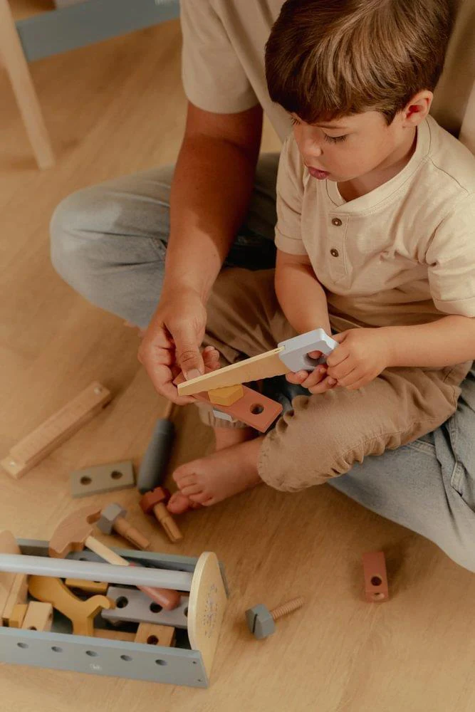 Criança e adulto com brinquedo de ferramentas em madeira colorida sentados no chão