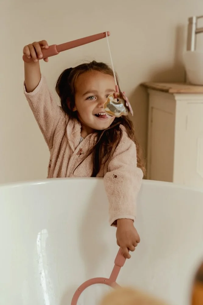 Menina a brincar numa banheira com vara de pesca de brinquedo rosa