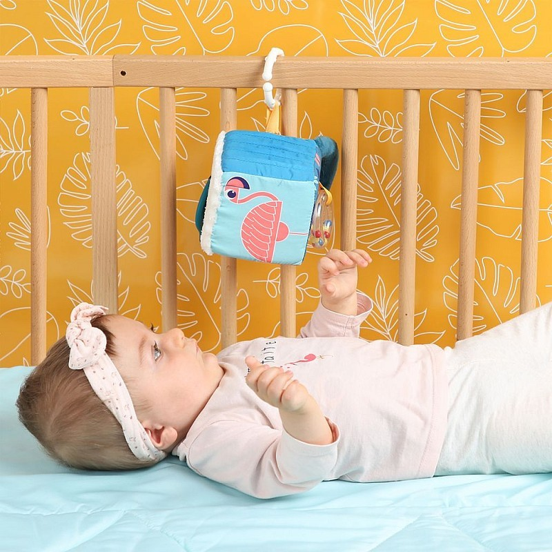 Cubo de tecido colorido com flamingo pendurado num berço, bebé deitado a olhar para o brinquedo