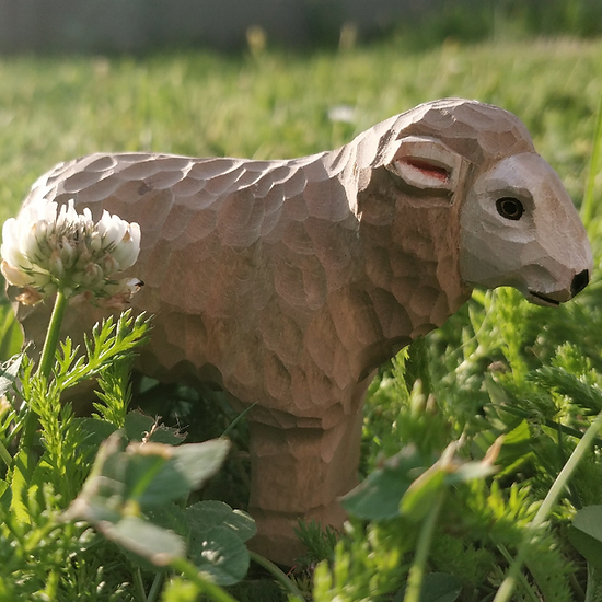 Figura de ovelha esculpida em madeira entre relva e flor branca