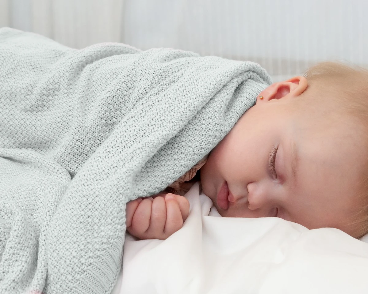 Bebé a dormir com manta cinzenta de malha fina
