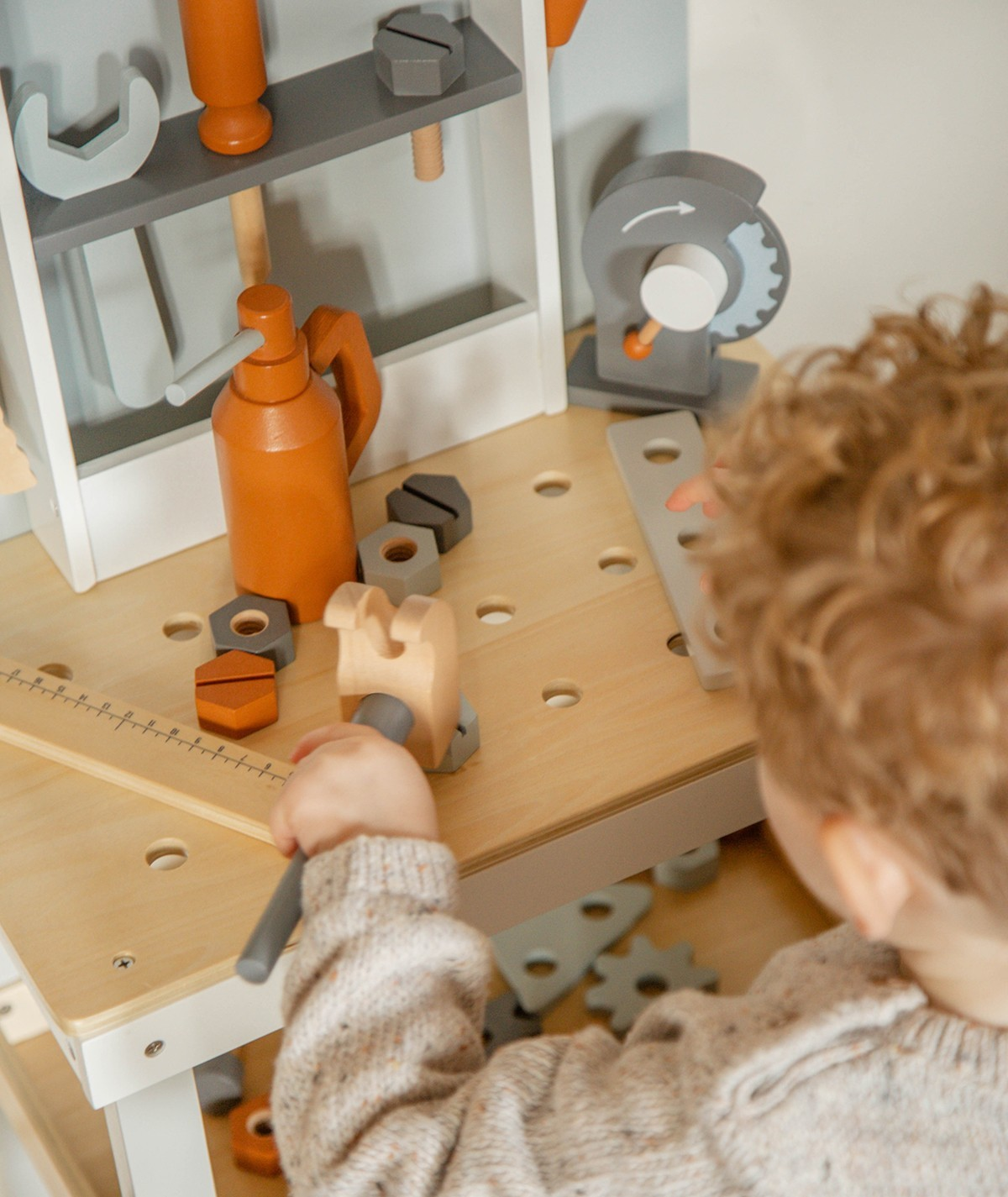 Criança a brincar com ferramentas de madeira numa bancada com furos circulares