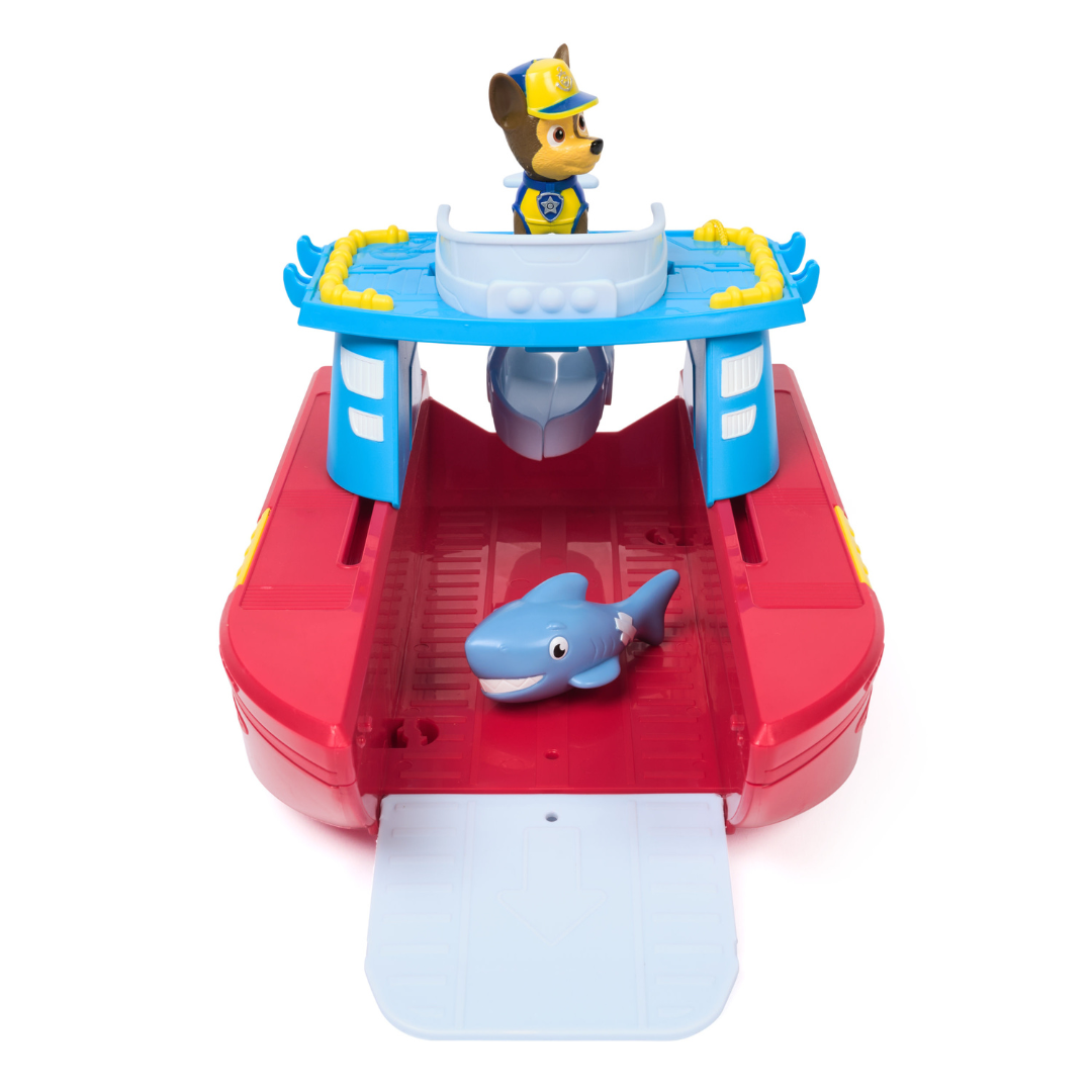 Brinquedo de barco vermelho e azul com figura de cão em uniforme e tubarão azul.