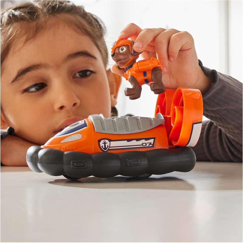 Criança a brincar com brinquedo hovercraft laranja e figura de cão de plástico.