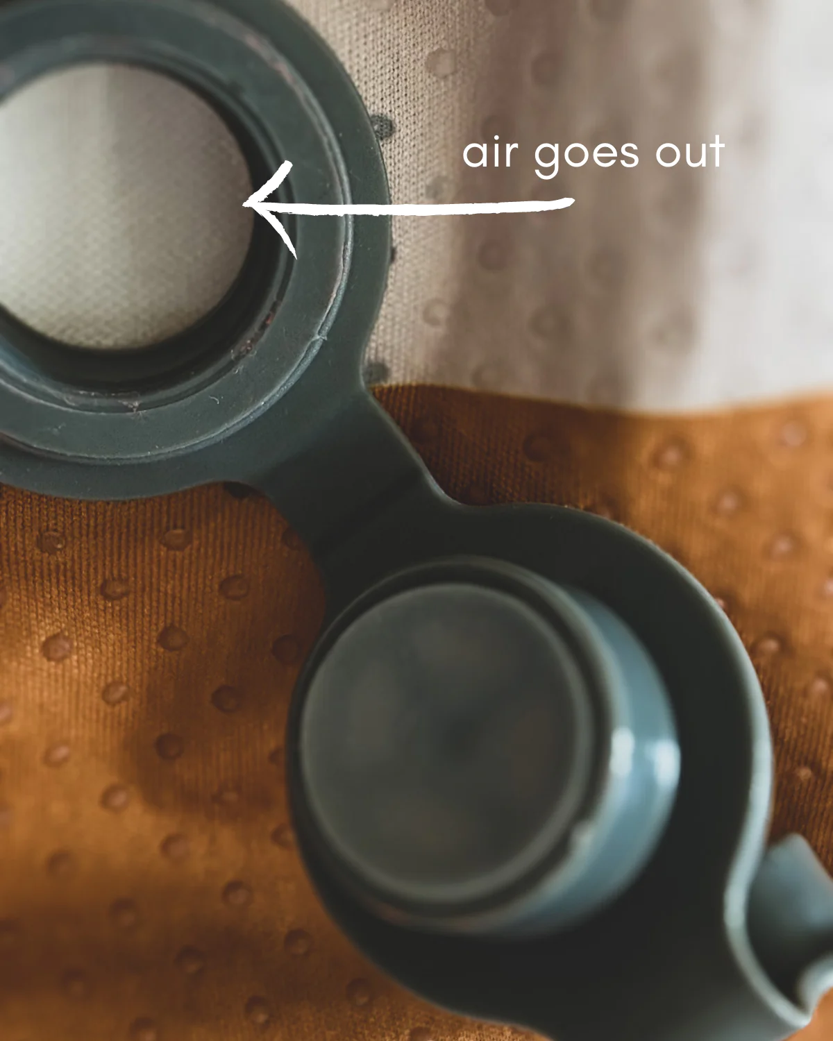 Peça de plástico com selo circular sobre tecido texturizado com texto 'air goes out'