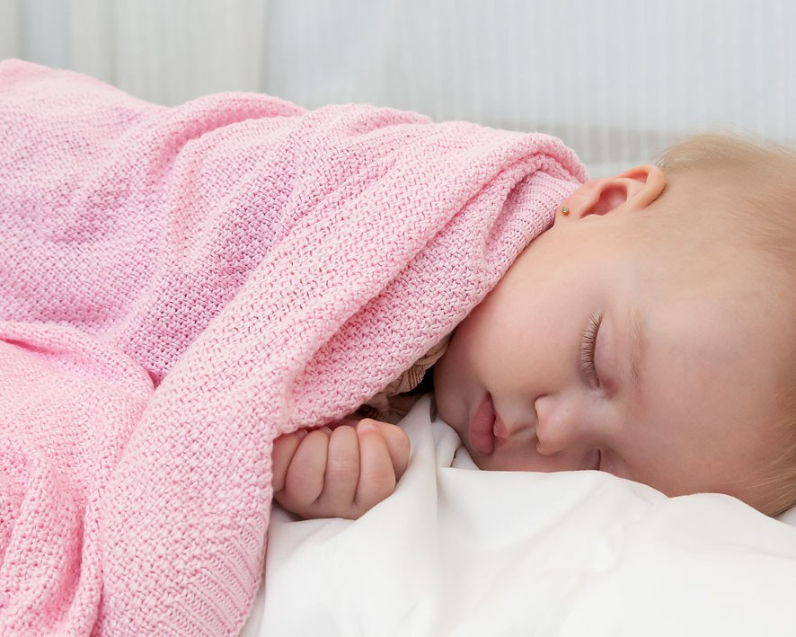 Bebé adormecido coberto com cobertor cor-de-rosa de malha