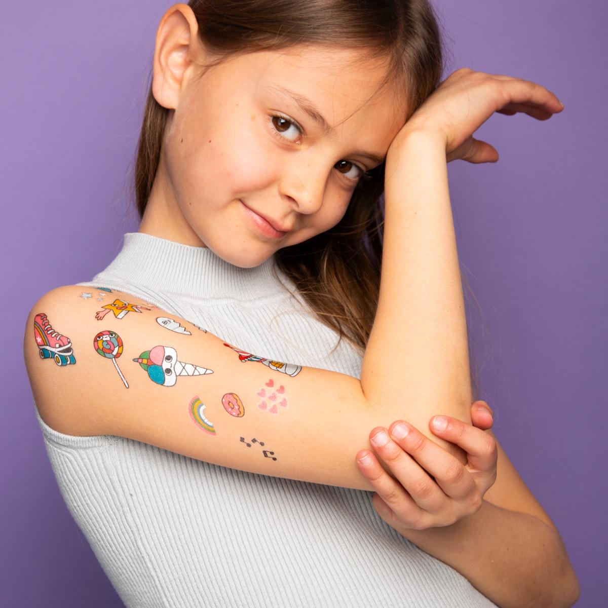 Menina com tatuagens temporárias coloridas no braço direito e camisola cinza claro