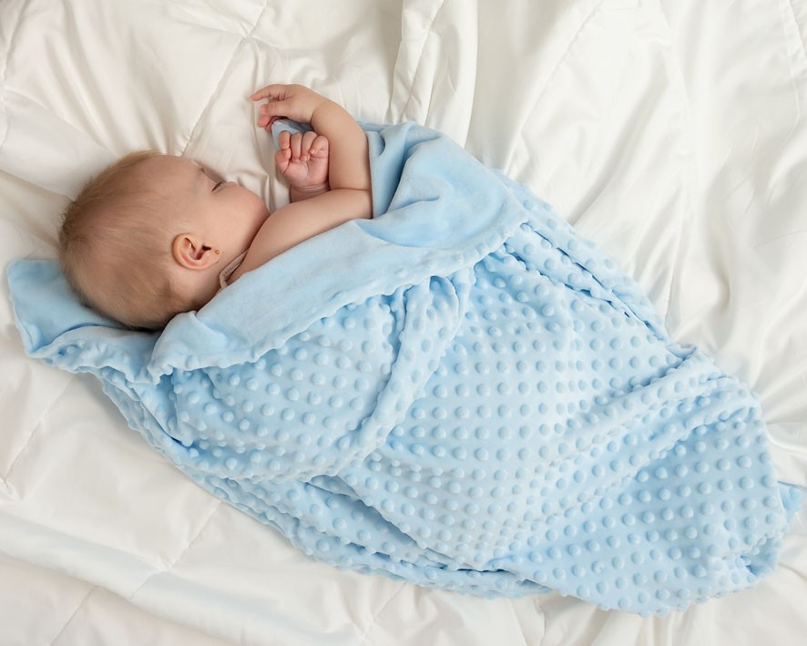 Bebé a dormir em manta azul com textura acolchoada sobre lençóis brancos