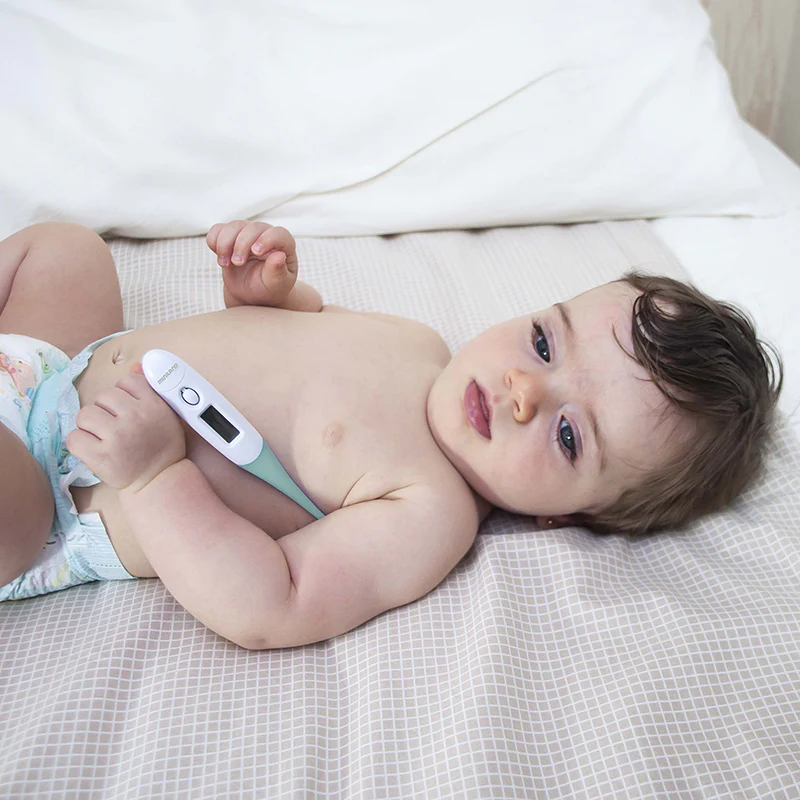 Bebé deitado com fralda segurando termómetro digital na cama