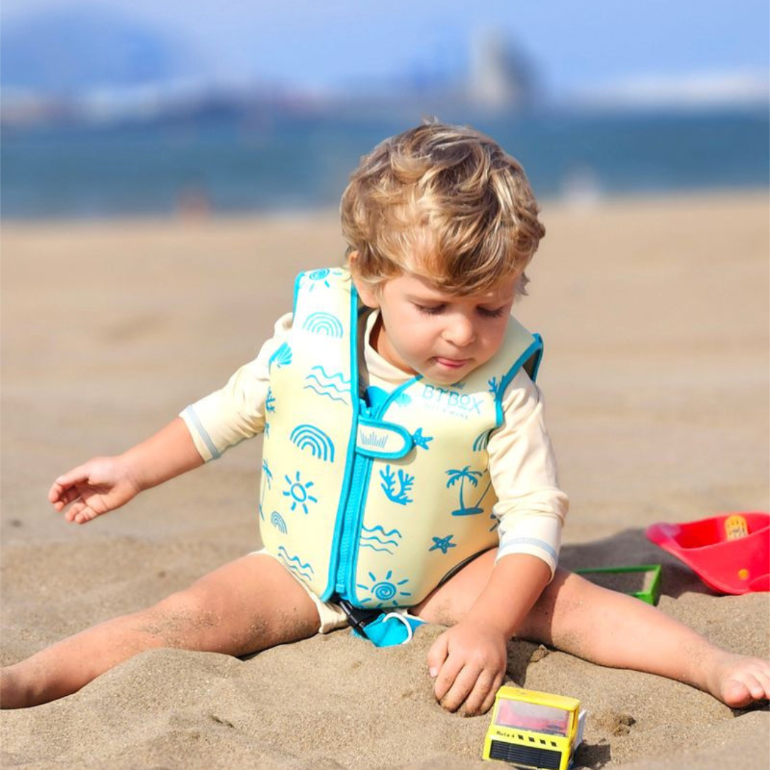 Criança na praia com colete salva-vidas amarelo e brinquedos na areia