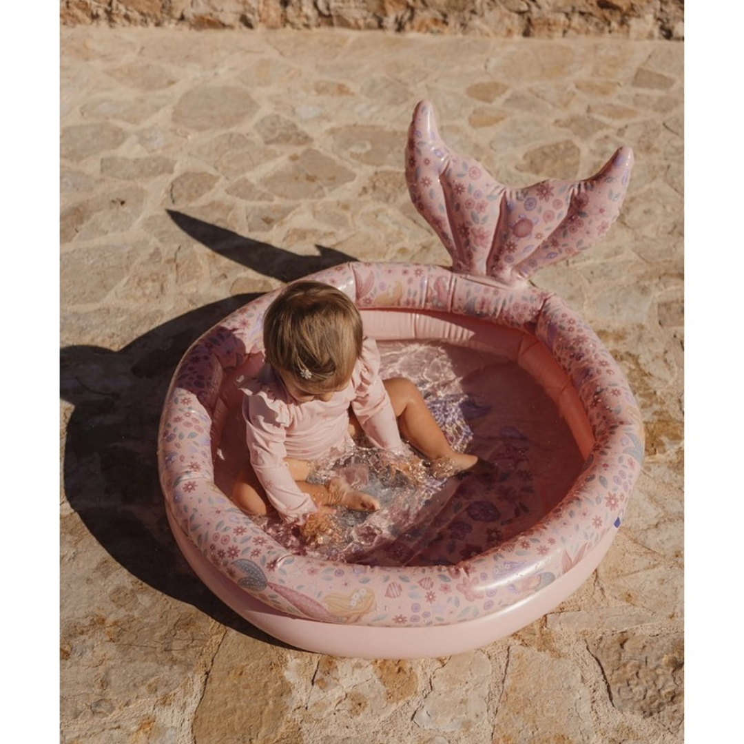 Piscina insuflável rosa com padrão floral para criança no chão de pedra com criança dentro