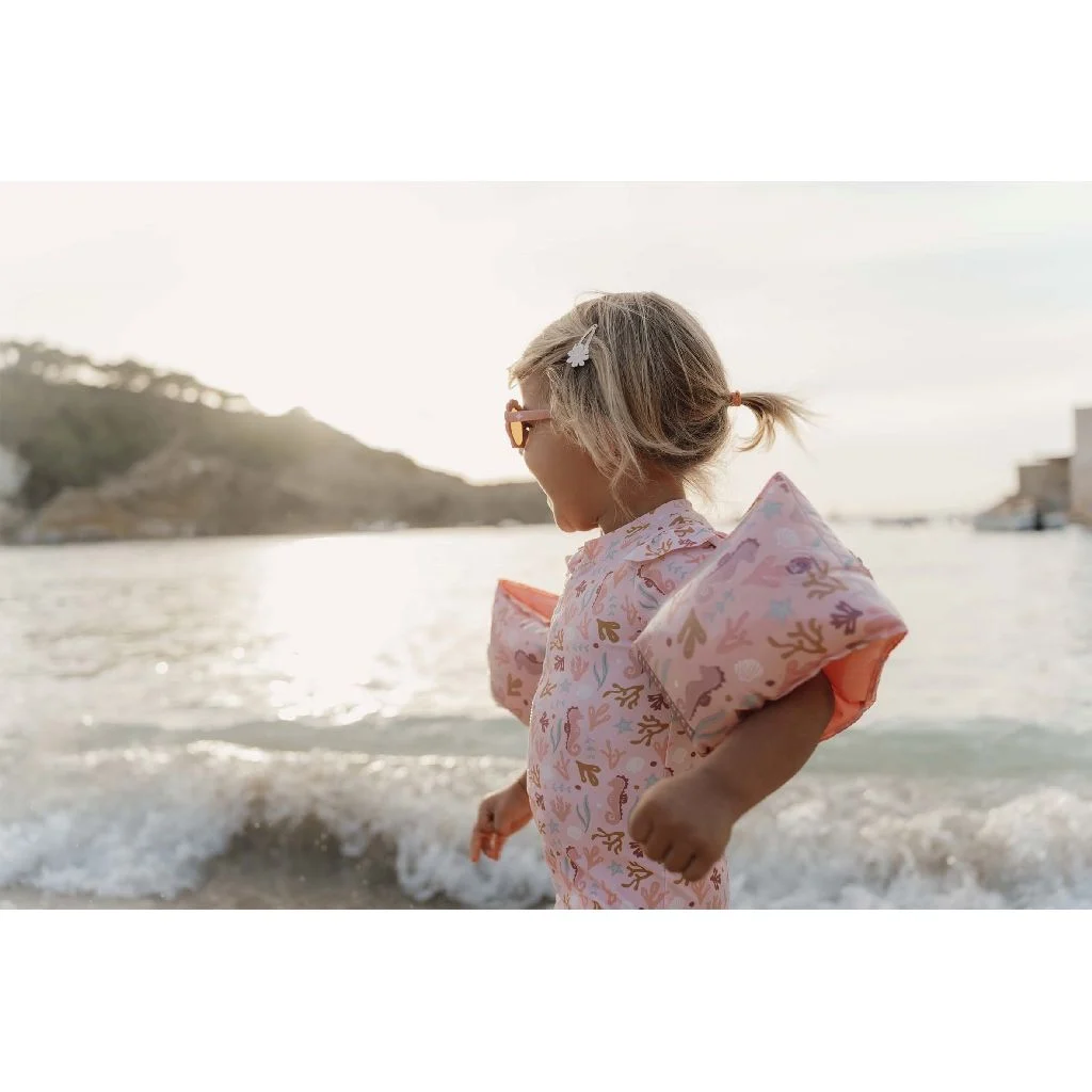 Criança com colete de salva-vidas rosa na praia