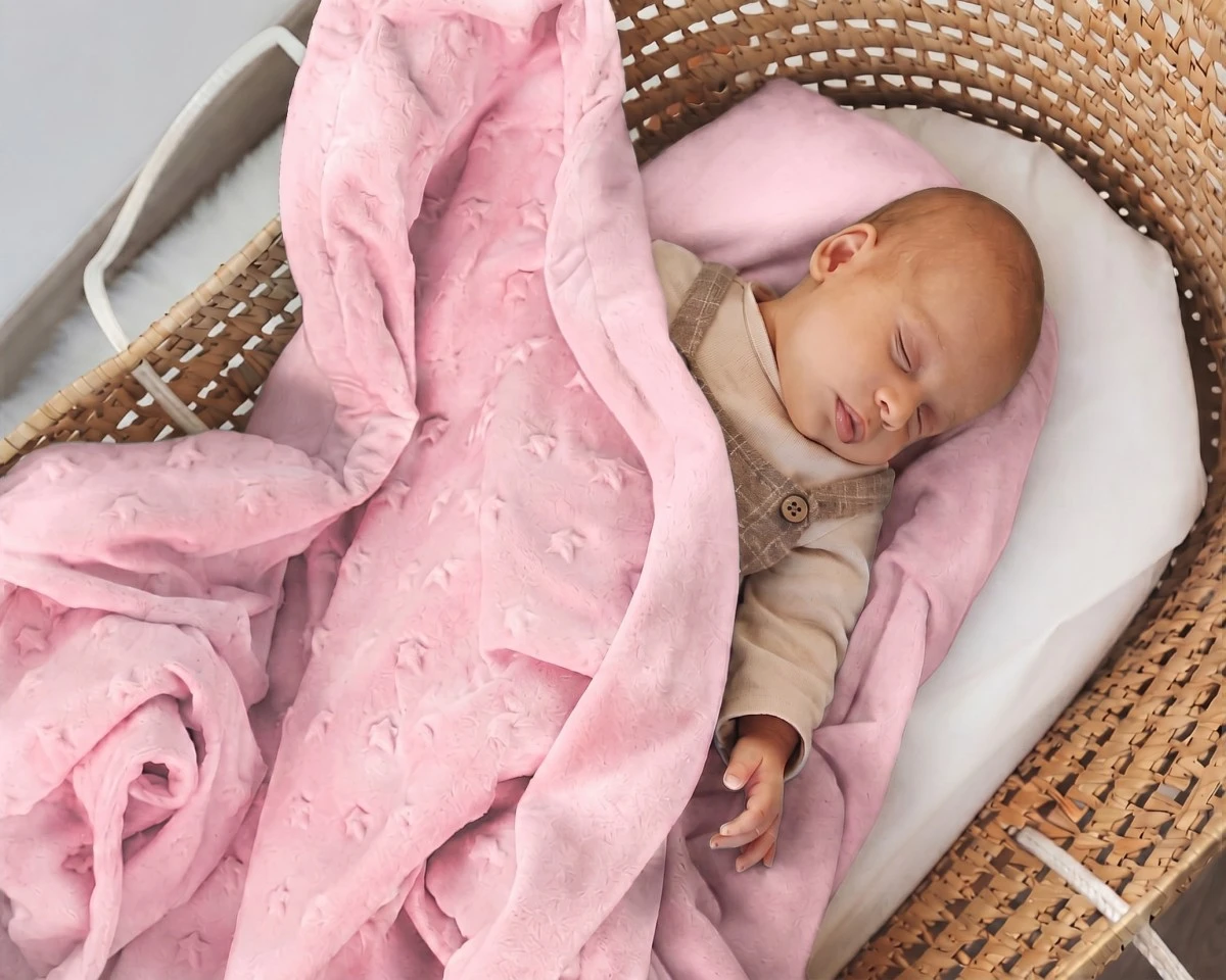 Bebé dorme num cesto com manta rosa e almofada cor-de-rosa.
