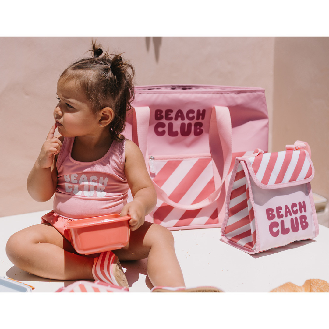 Criança com fato de banho rosa e mochila e lancheira rosas com texto BEACH CLUB