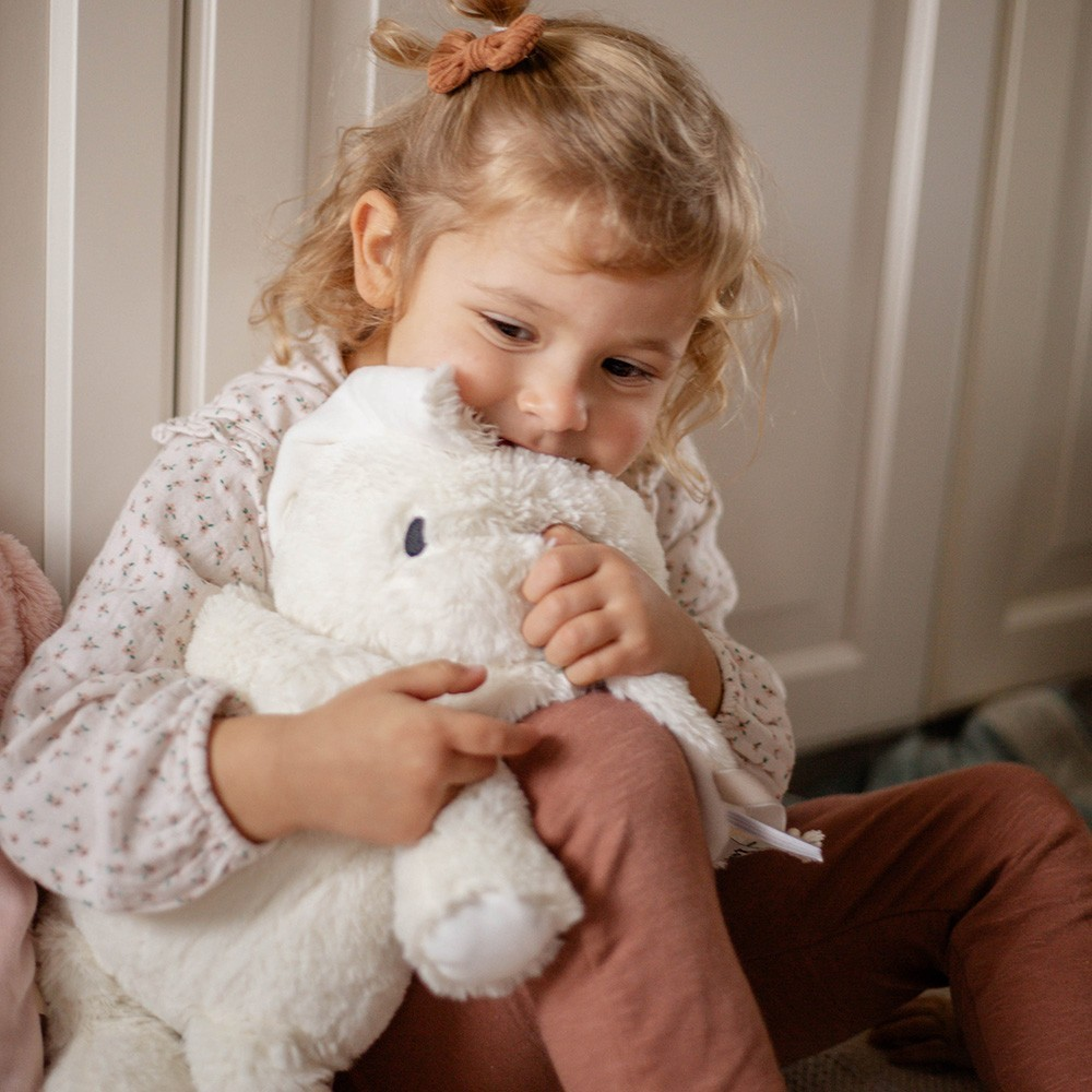 Criança loira abraçando peluche branco num quarto interior