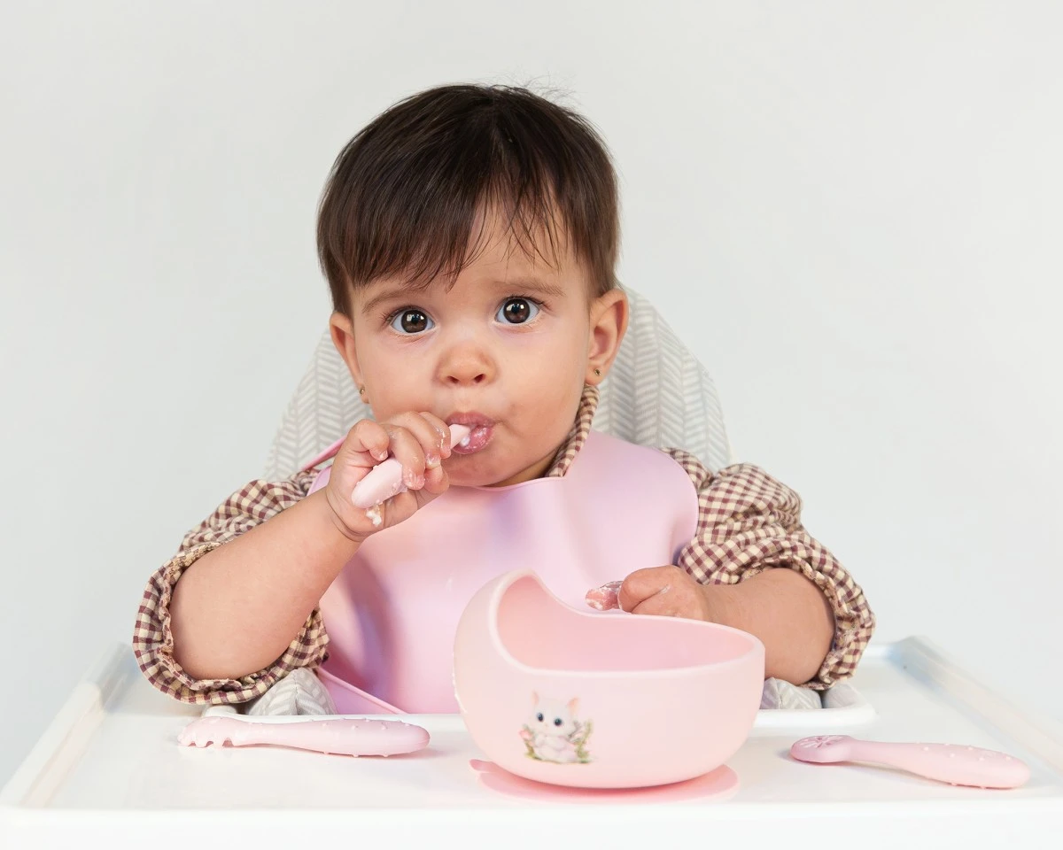 Bebé com babete rosa a comer em cadeira alta