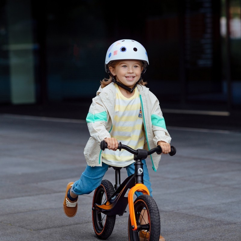 Criança com capacete branco e bicicleta de equilíbrio laranja e preta