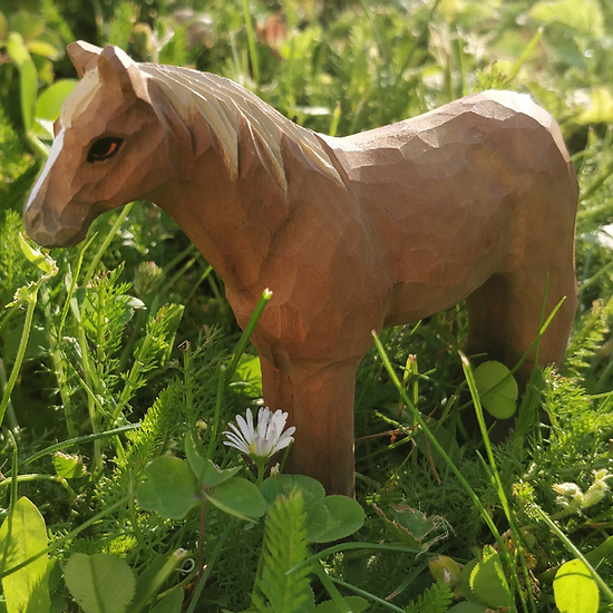 Estatueta de cavalo em madeira sobre relva verde com flores brancas