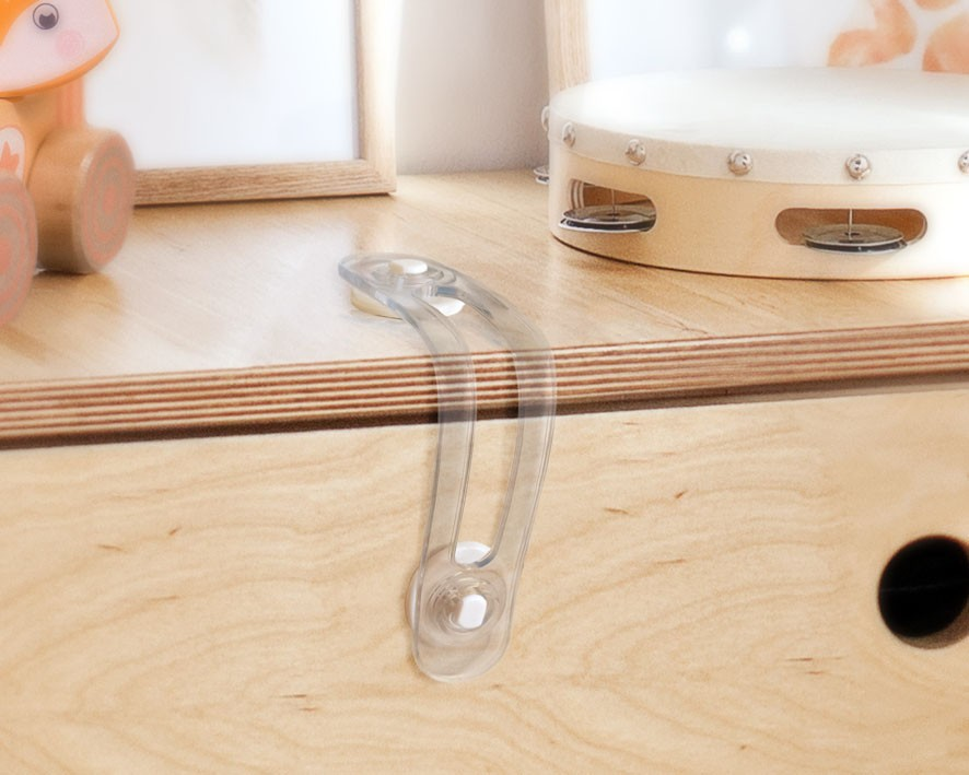Trava de segurança transparente num móvel de madeira clara com pandeiro branco ao fundo.