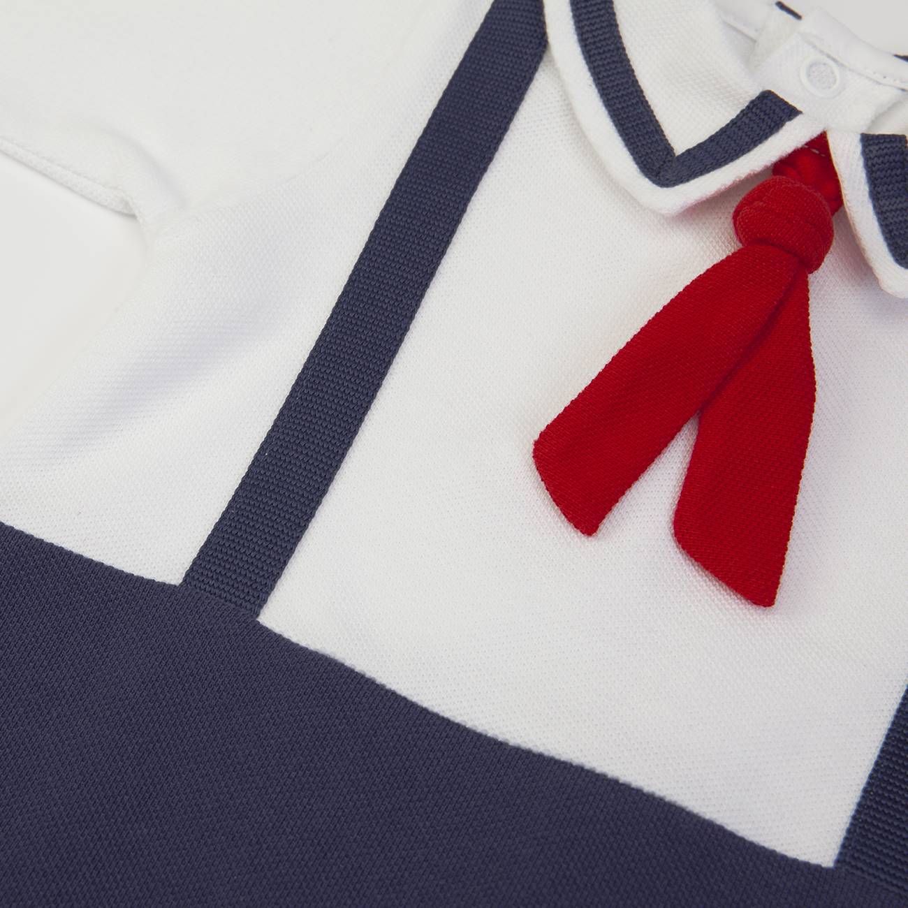 Roupa de criança branca e azul escuro com laço vermelho.