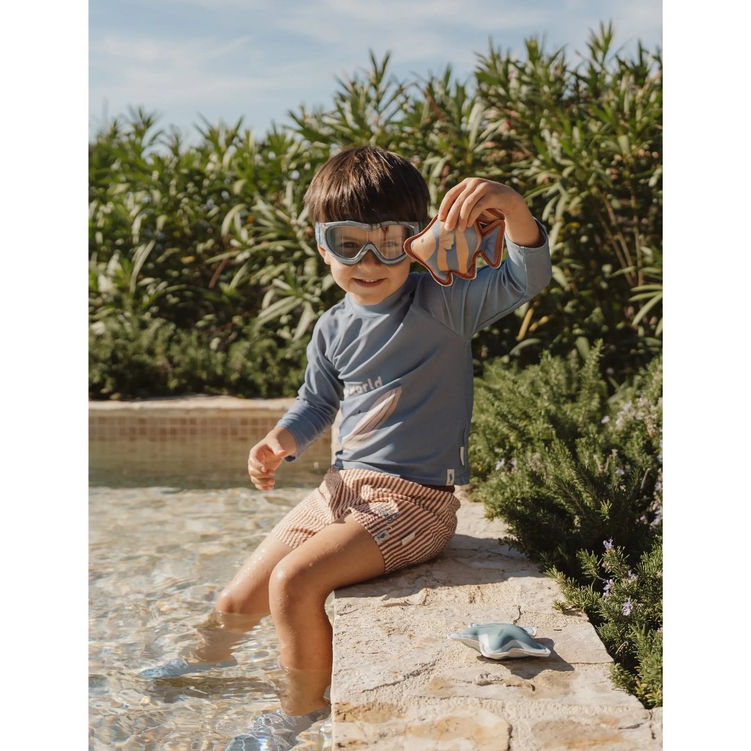 Criança com roupa de banho e óculos de mergulho junto a piscina segurando brinquedo de peixe