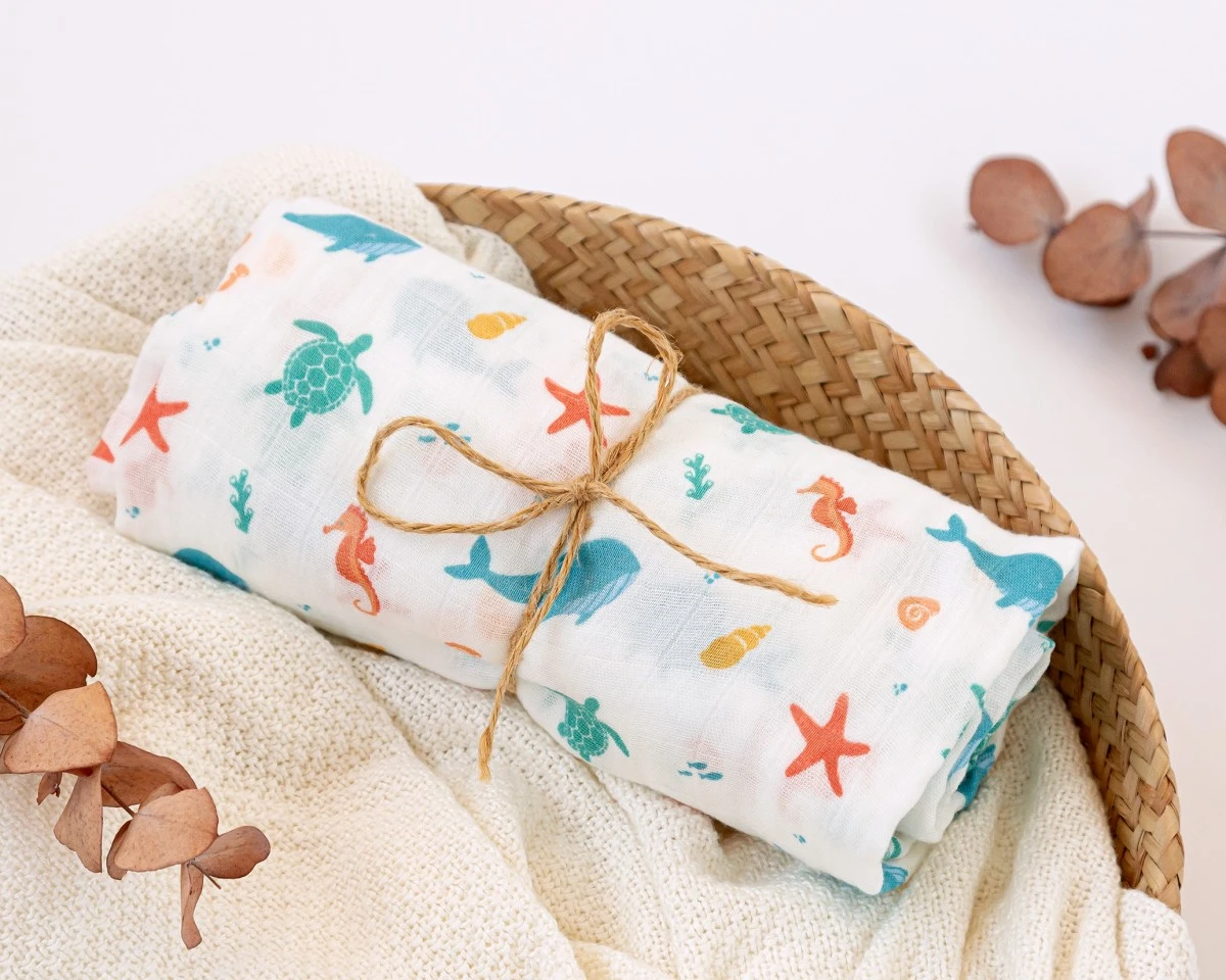 Fralda ou manta infantil com estampas marinhas coloridas, amarrada com cordão de ráfia numa cesta de vime