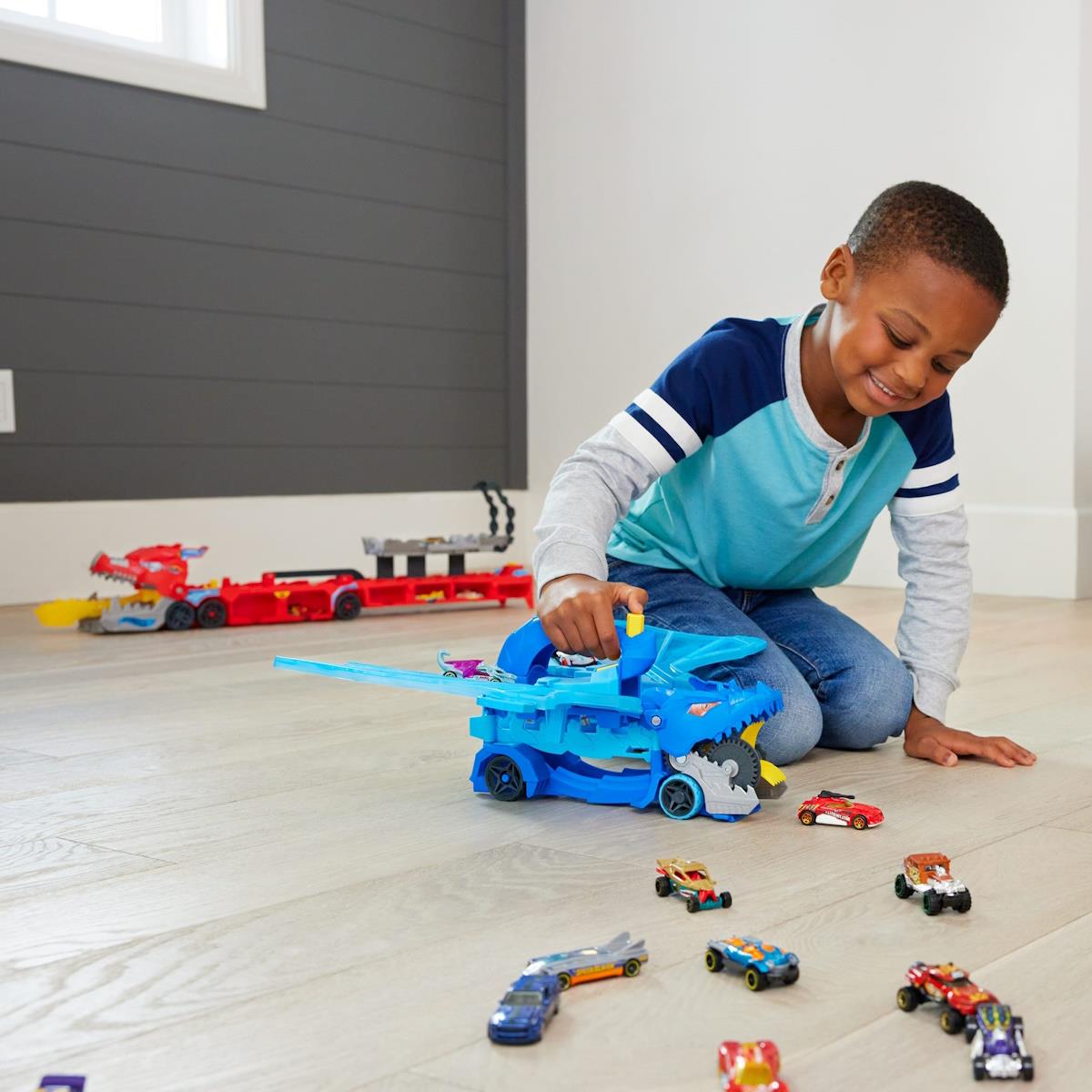 Menino a jogar com autocarro de brinquedo azul e carrinhos numa sala com parede cinzenta.