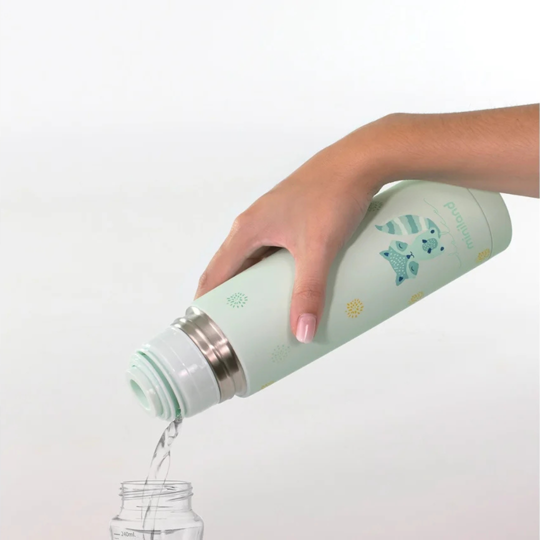 Garrafa térmica verde claro com desenhos de animais vertendo água para jarro transparente.