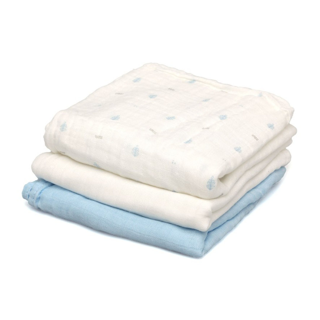 Três panos de algodão, branco com padrões azuis, branco liso e azul claro empilhados.