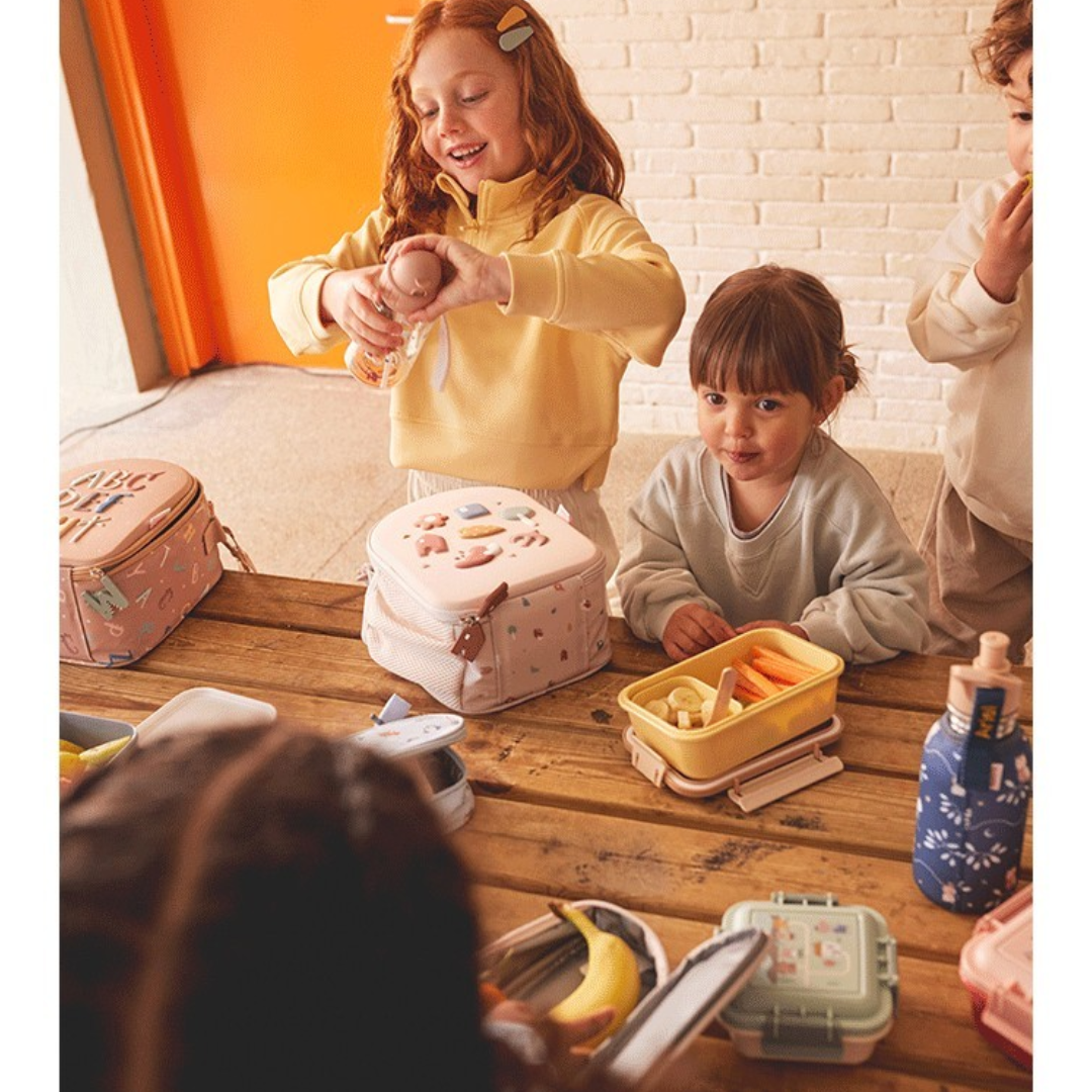 Lancheiras coloridas e alimentos numa mesa de madeira com crianças ao redor