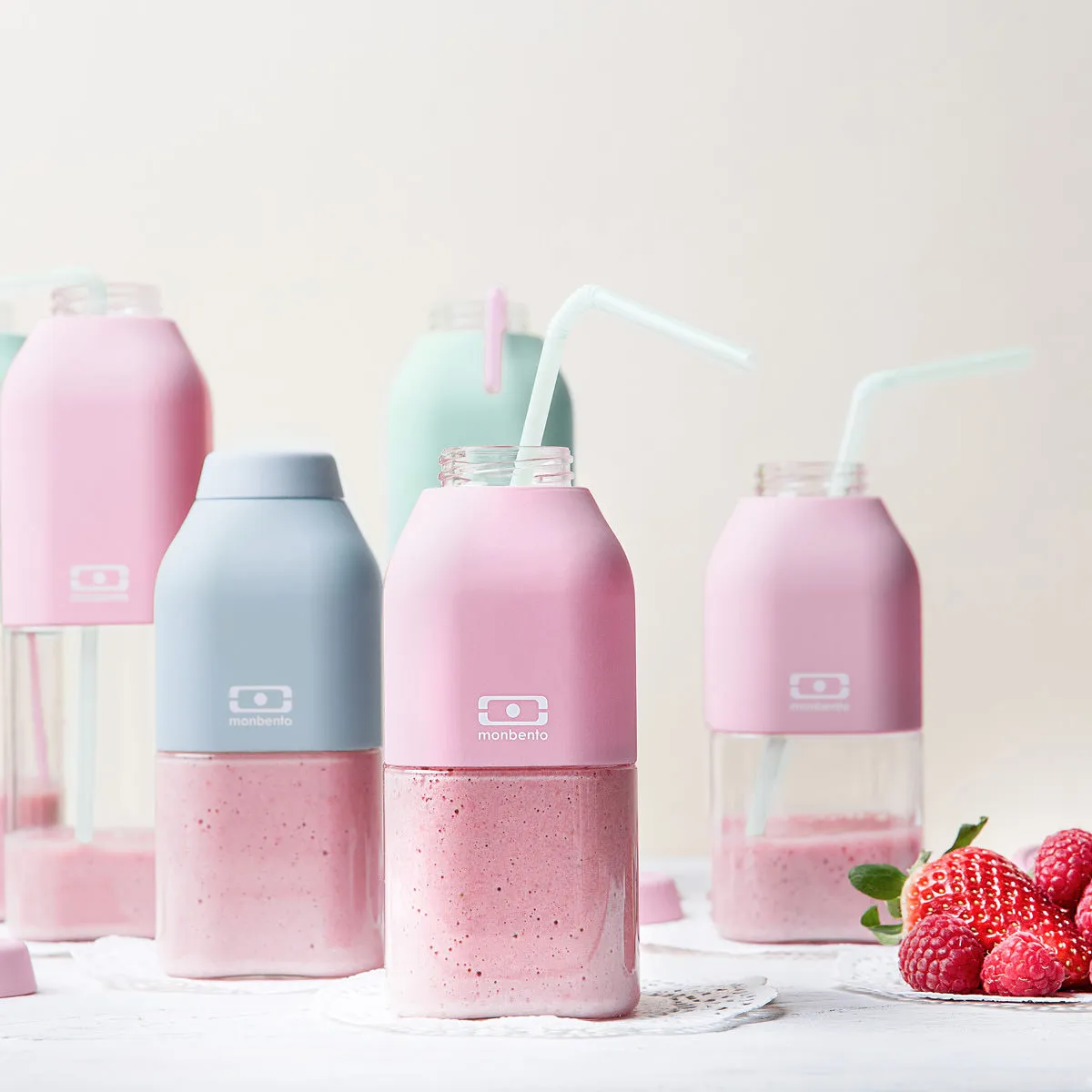 Garrafas monbento em cor pastel com batidos cor de rosa e frutas frescas ao lado