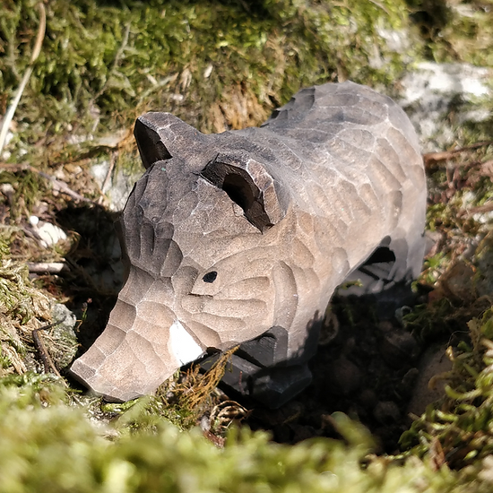 Figurinha esculpida de um porco em madeira com textura facetada sobre musgo e pedras