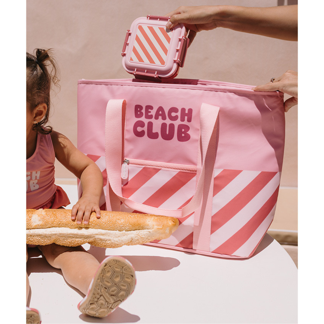 Mala rosa BEACH CLUB com padrão riscas e criança segurando baguete