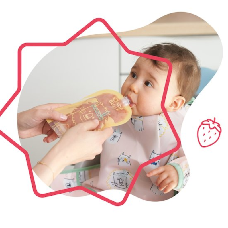 Criança a ser alimentada com saqueta amarela, usando babete rosa com gatos