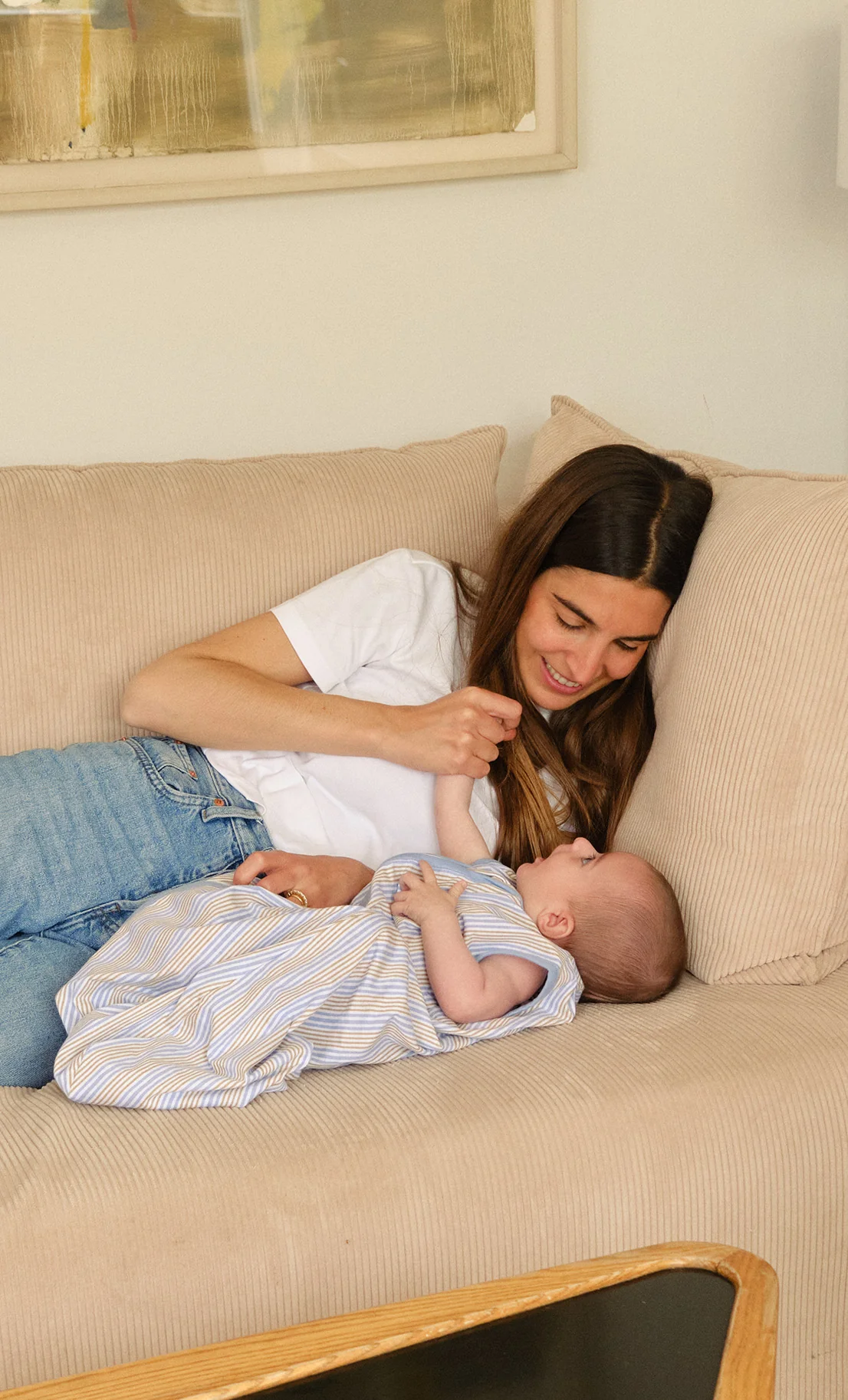 Mulher e bebé deitados num sofá bege com textura canelada.