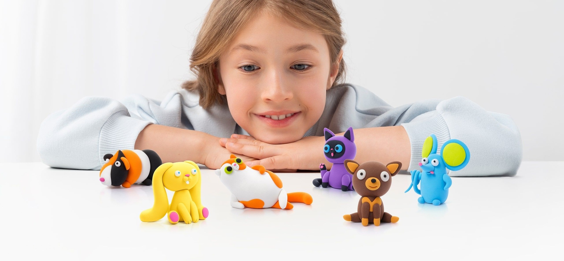 Criança com brinquedos coloridos de animais de material moldável numa mesa branca