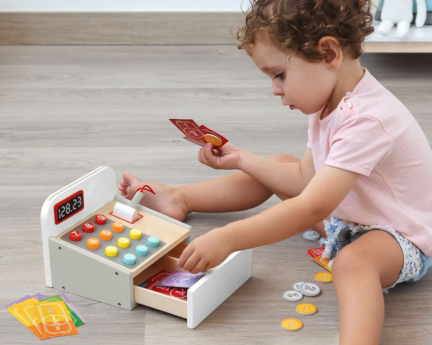Criança brinca com caixa registadora de brinquedo colorida em madeira no chão