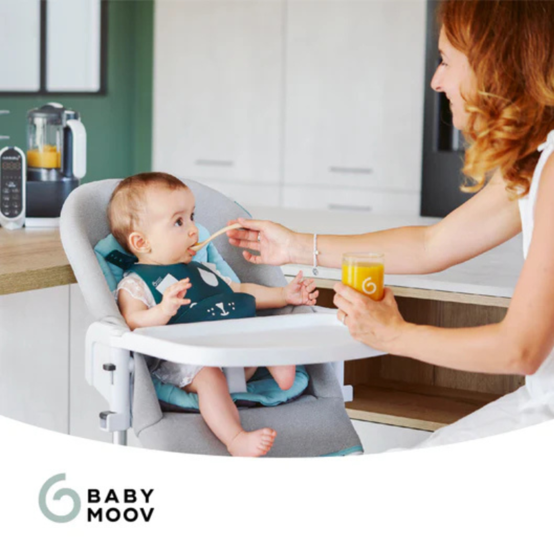 Bebé sentado em cadeira alta cinzenta a ser alimentado por mulher em cozinha