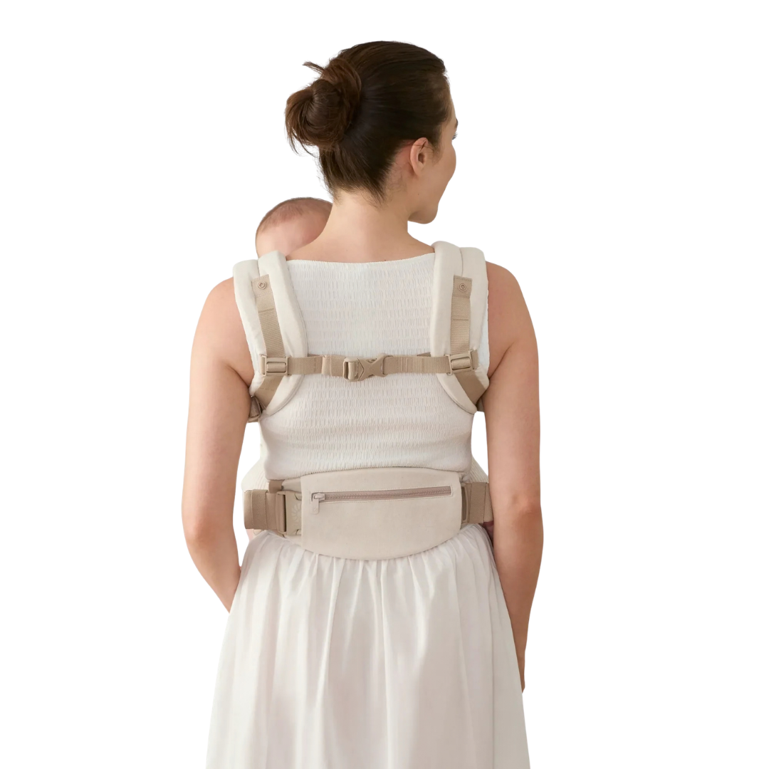 Canguru ergonómico bege com fecho, usado por mulher vista de costas com vestido branco.