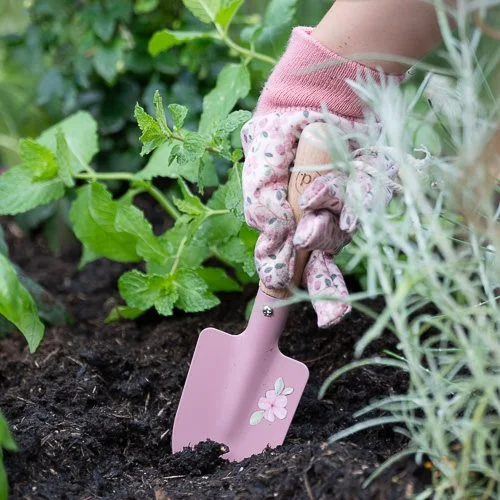 Pá de jardinagem rosa com flor pintada e luva rosa a trabalhar em terra