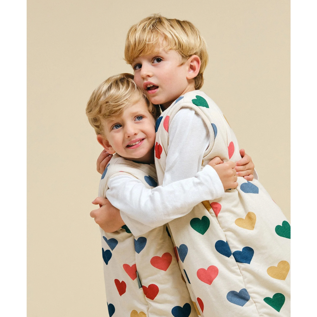 Duas crianças a abraçar com pijamas creme estampados de corações coloridos.