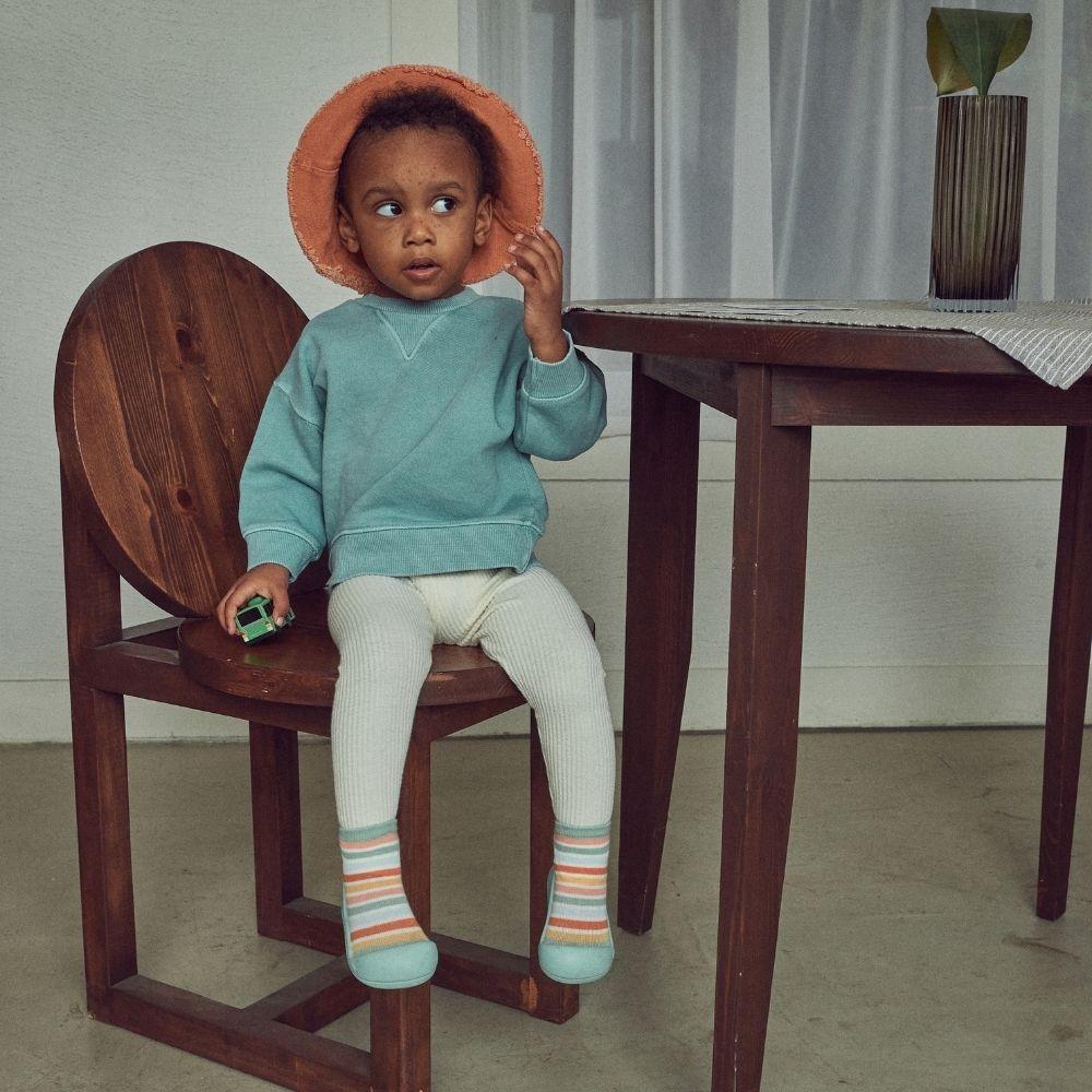 Criança com roupa colorida sentada numa cadeira de madeira escura