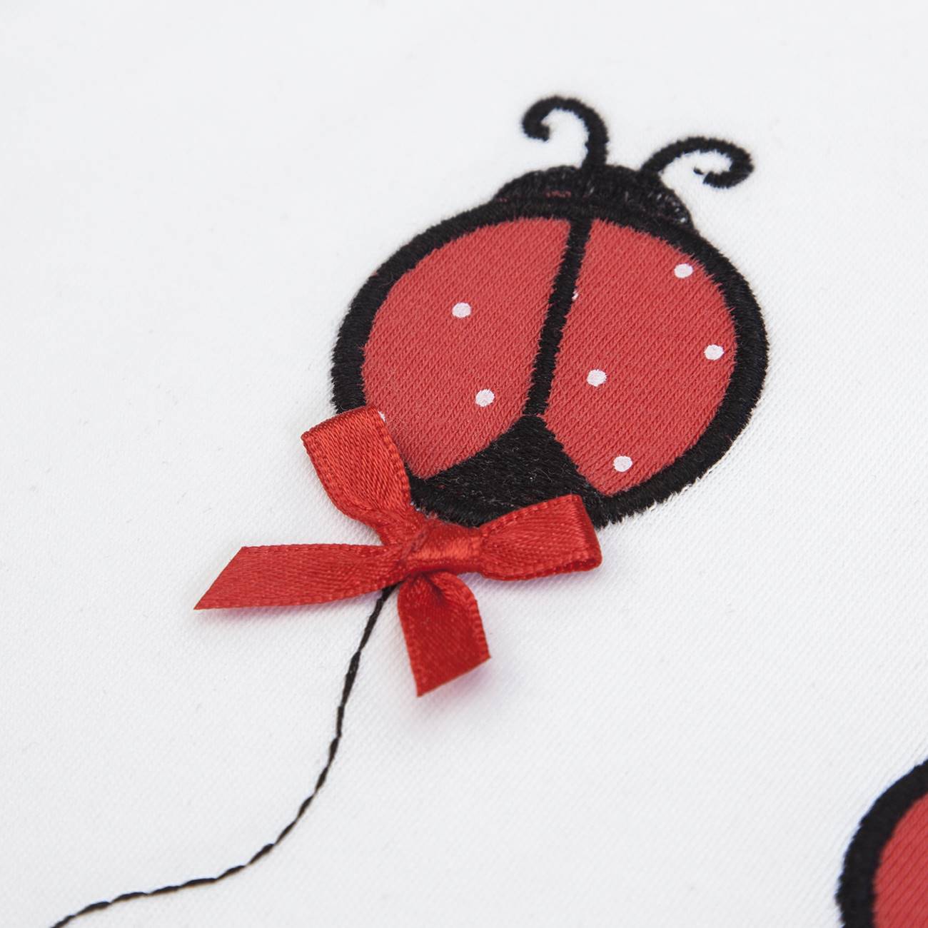 Joaninha bordada em tecido branco com laço vermelho