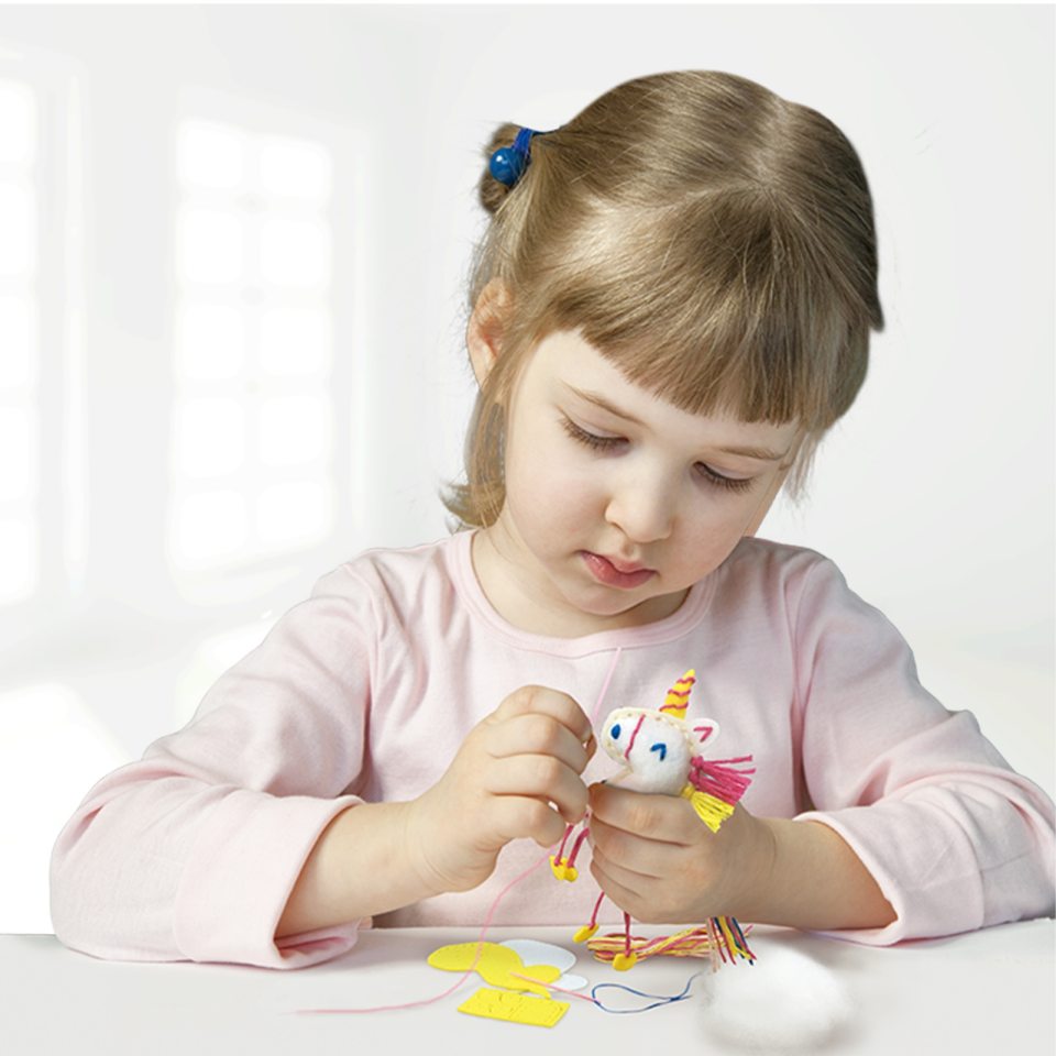 Menina a fazer trabalhos manuais com boneco de feltro unicórnio colorido