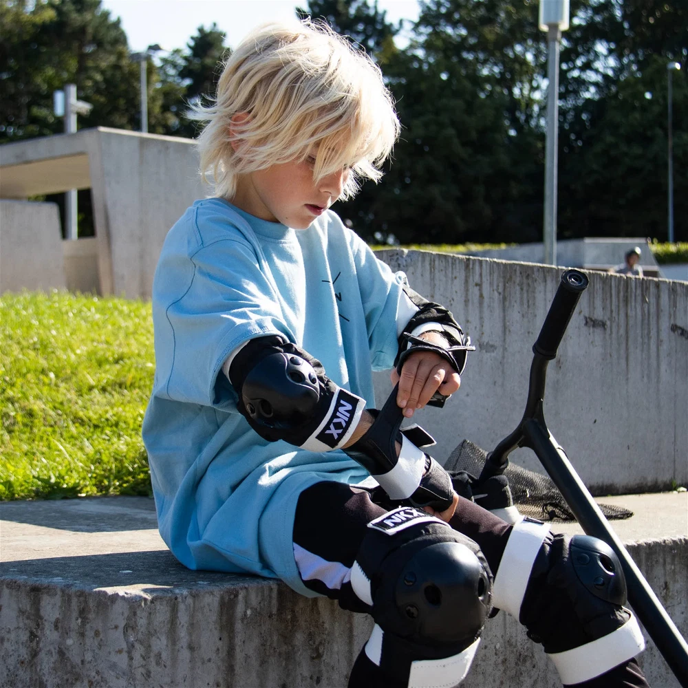 Criança com equipamento de proteção e patinete sentado num muro exterior
