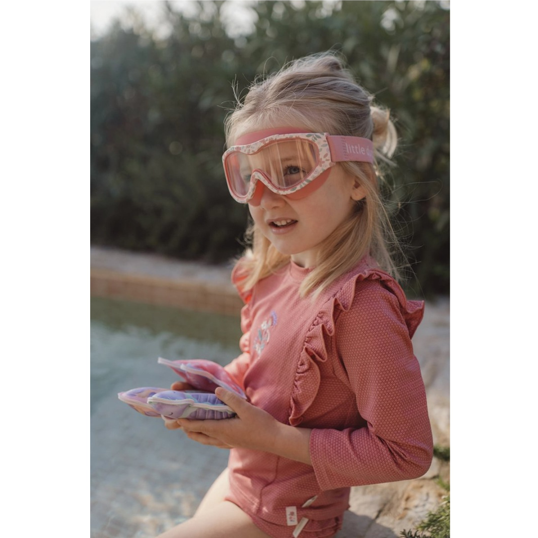 Menina com fato de banho rosa e óculos de proteção rosa junto à piscina
