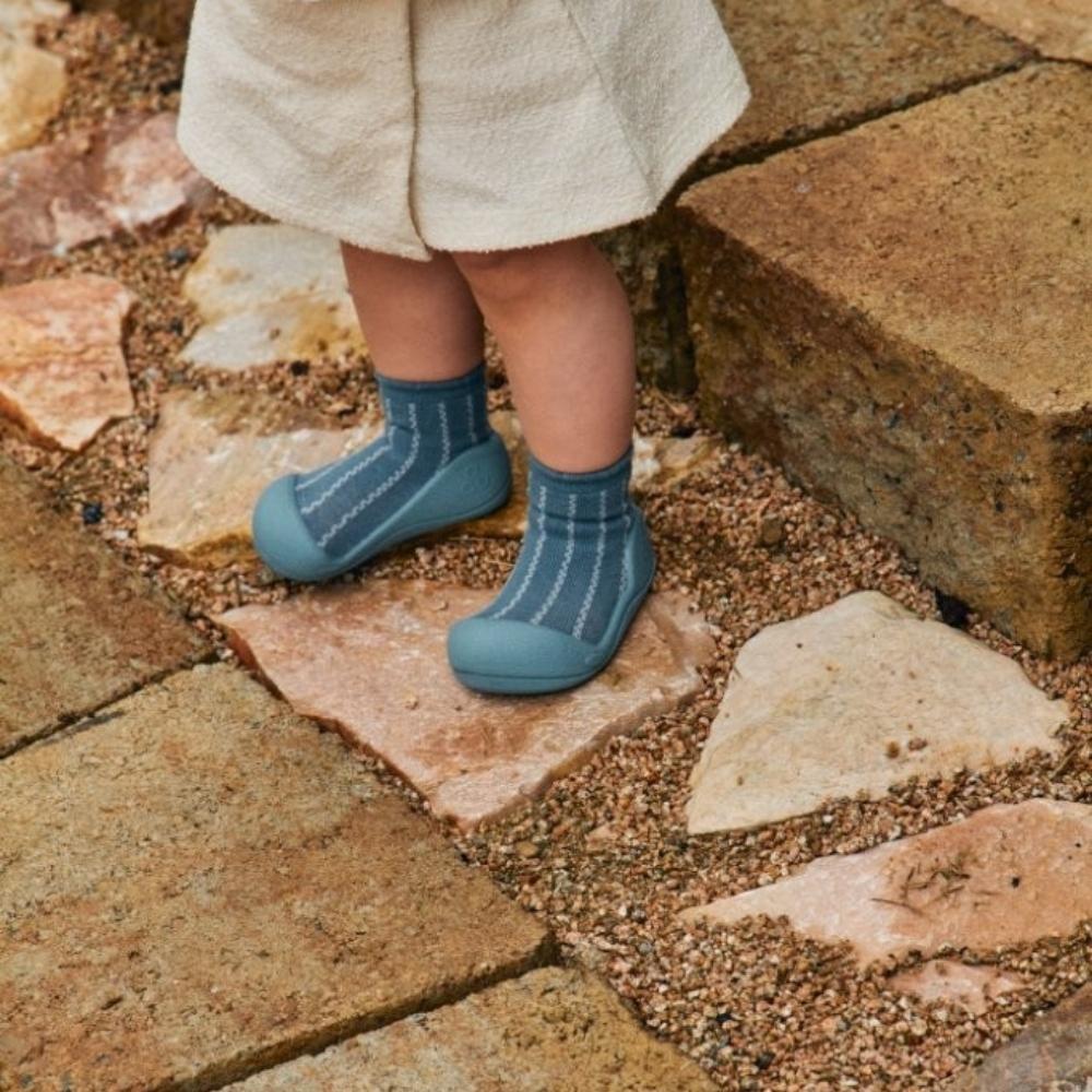 Sapatos para bebé azul com padrão branco em chão de pedras e terra